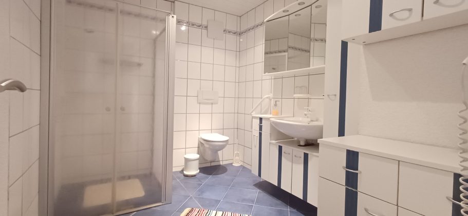 Badezimmer Helles Badezimmer mit Dusche, Toilette, Waschbecken und blauem Boden.