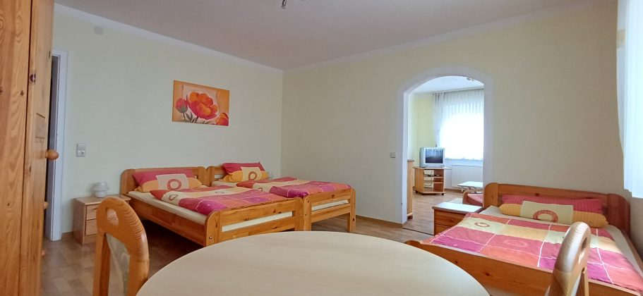 3 Bett Zimmer Helles Zimmer mit drei Betten, Tisch und Stühlen, freundliche Farbgestaltung.