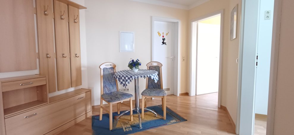 Heller Flur mit Tisch und Stühlen, Holzschränken und heller Wandgestaltung.