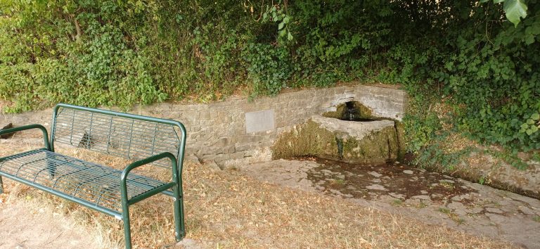 Der historische Ittlinger Brunnen in Sinsheim Weiler Historic Ittlinger Brunnen in Sinsheim-Weiler: Rustikaler Sandsteinbrunnen mit plätscherndem Wasser, Gedenktafel und grüner Bank.