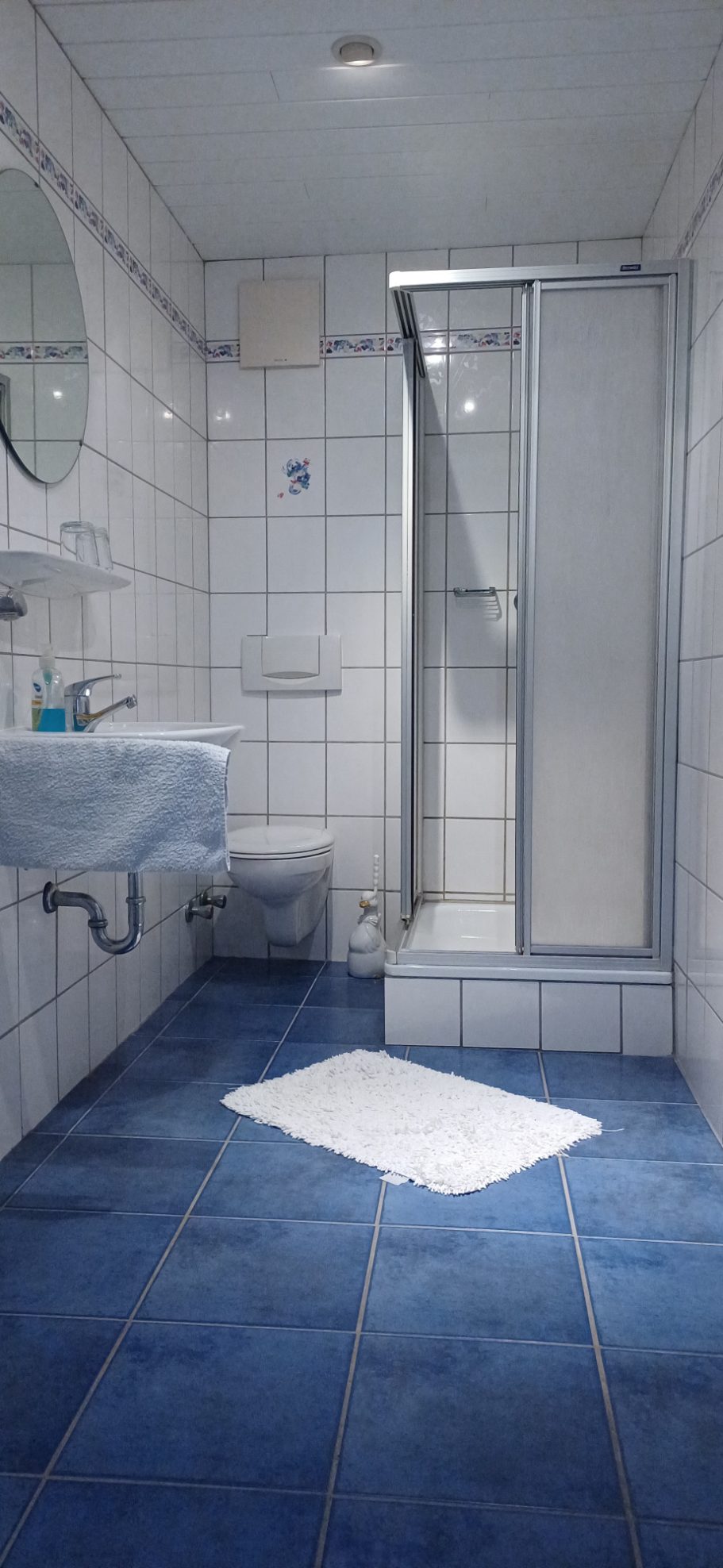 Badezimmer auf der Etage Badezimmer mit Dusche, Waschbecken, WC und blauem Fliesenboden.