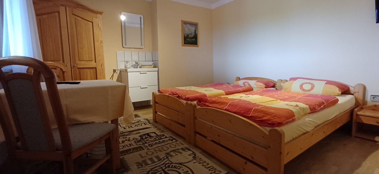 Gemütliches Zimmer mit zwei Betten, Tisch und Holzschränken. Helle, einladende Atmosphäre.