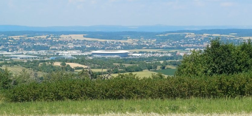 Weite Landschaft mit sanften Hügeln und einem Blick auf die Stadt im Hintergrund.