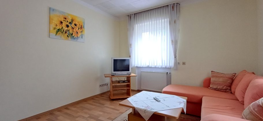 Wohnzimmer Heller Wohnraum mit Couch, Tisch und Fernseher, goldene Sonnenblumenmalerei an der Wand